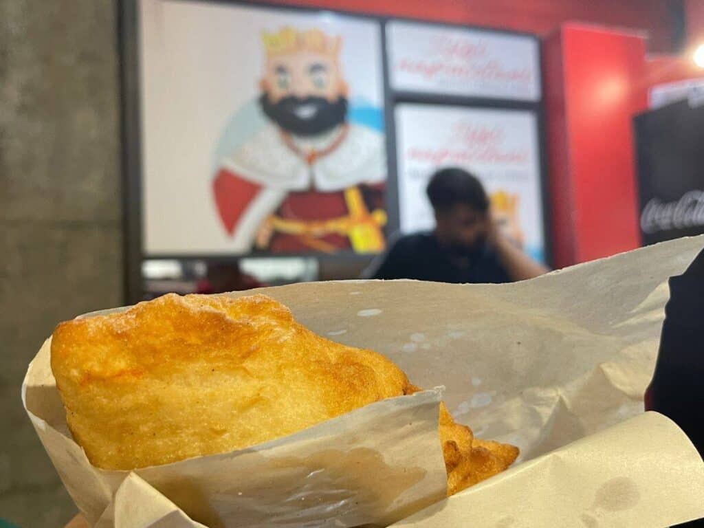 Piece of fried pizza in a paper cone in front of a graphic showing the king of Naples