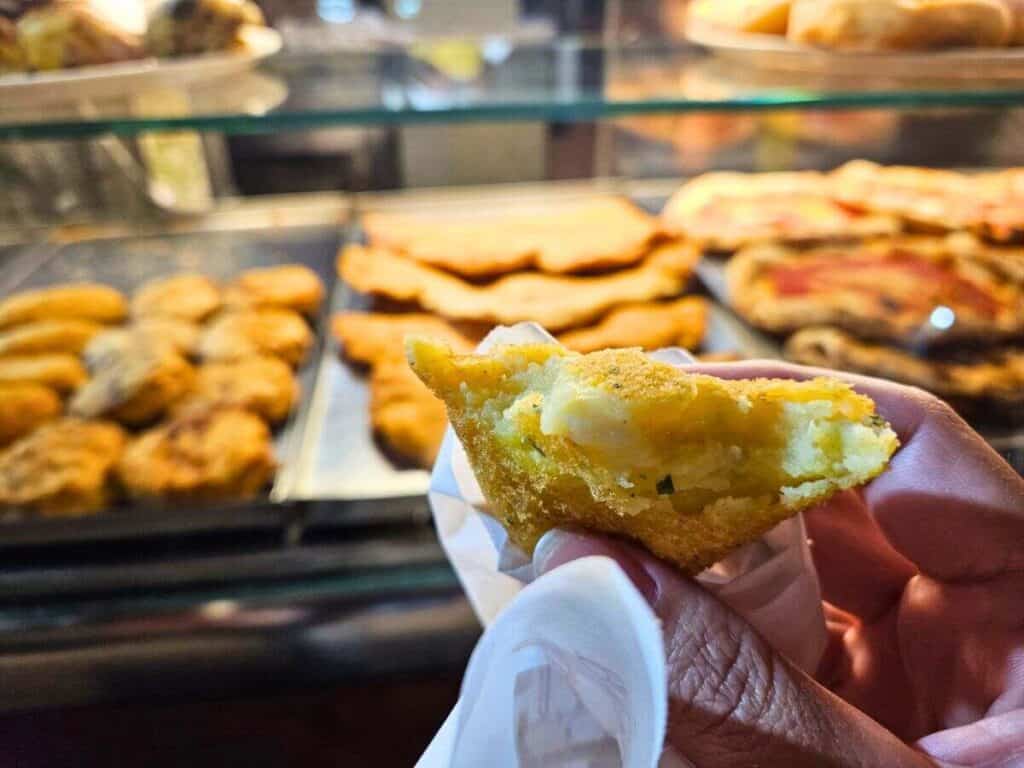 Author Christina holding a fried, vegetarian piece filled with cheese and potato in front of a counter full of fried street food.